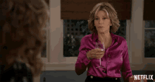 a woman in a pink satin blouse is holding a glass of wine in front of a netflix logo