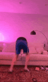 a man in blue shorts is doing a handstand in front of a couch