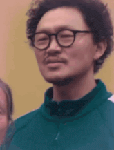 a man with a beard and glasses is wearing a green jacket and smiling .
