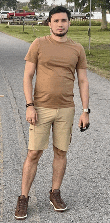 a man wearing a brown shirt and khaki shorts is standing on a road