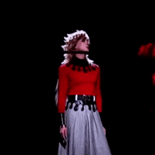a man in a red sweater and gray skirt is standing on a stage in a dark room .