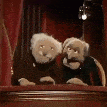 two muppets are sitting next to each other on a stage in front of a microphone .