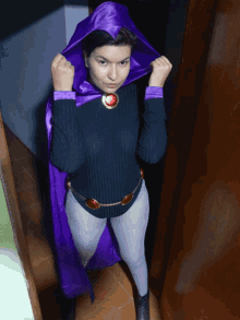 a woman wearing a black sweater and a purple cape is standing in a hallway