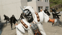 a group of people are standing in front of a building and one of them is wearing a mask with the letter o on it