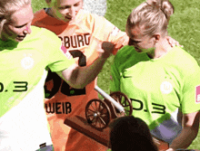 three female soccer players wearing green and orange jerseys with the number 3