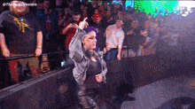 a woman with purple hair is standing in front of a crowd and giving the middle finger