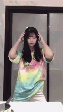 a woman wearing a tie dye shirt and a hat is standing in front of a glass door .