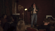 a man singing into a microphone in front of a crowd with a red curtain