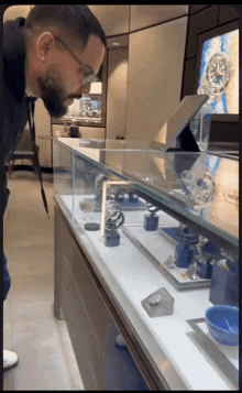 a man wearing glasses looks at a watch in a glass case