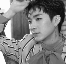 a black and white photo of a young man wearing earrings and a bow tie