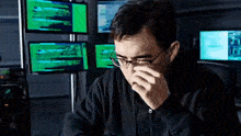 a man wearing glasses is sitting in front of a bunch of monitors