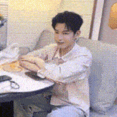 a young man is sitting at a table with his arms crossed and looking at his phone .