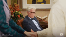 a man in a suit and bow tie is sitting in a chair while a woman holds his hand .