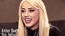 amber heard is smiling while wearing a black top and red lipstick .