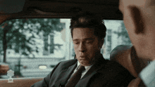 a man in a suit and tie is sitting in the back seat of a car with a chef logo on the side
