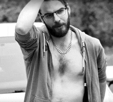 a shirtless man wearing glasses and a chain around his neck is standing next to a car