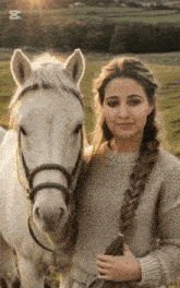 a woman stands next to a white horse with the letter x on the bottom