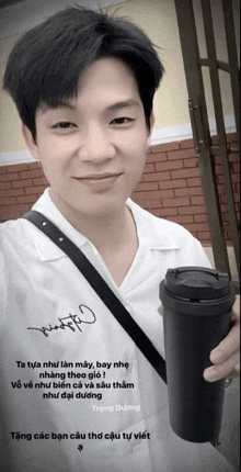 a man in a white shirt is holding a black coffee cup with a signature on the front