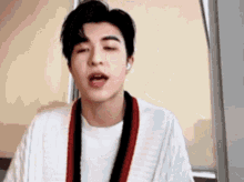 a young man wearing a white shirt and a red and black sweater is singing .