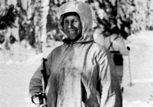 a black and white photo of a man wearing a hooded jacket and holding a gun in the snow .