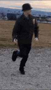 a man in a hat and jacket is running on a gravel path .