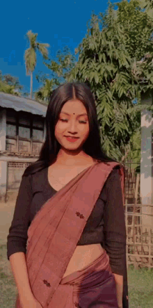 a woman in a saree and a black shirt is standing in front of a building .
