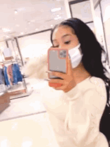 a woman wearing a face mask is taking a selfie in a mirror .