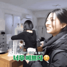 a woman in a black jacket stands next to another woman in a black jacket in a room with korean writing on the wall