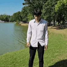 a man in a white shirt is standing near a lake