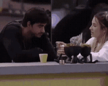 a man and a woman are sitting at a table looking at a cell phone