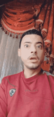 a man in a red shirt is making a surprised face .