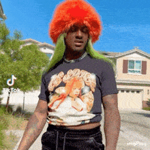 a man with green hair and an orange wig is wearing a black shirt with a picture of a woman on it