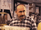 a bald man with a mustache wearing a plaid shirt is standing in a store