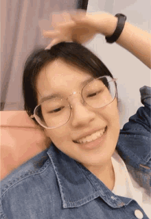 a girl wearing glasses and a denim jacket smiles for the camera
