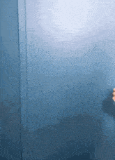 a person 's hand is reaching out towards a blue wall