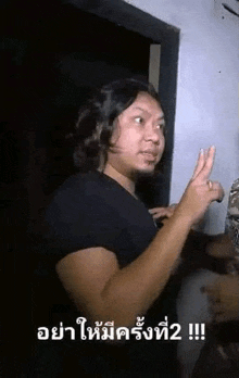 a man with long hair and a beard is standing in a dark room and making a peace sign .