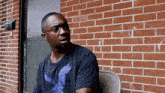 a man wearing glasses and a shirt with an eagle on it sits in front of a brick building