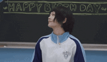 a girl is sitting at a desk in front of a blackboard that says birthday