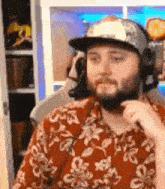 a man with a beard is wearing a hat and headphones while sitting in front of a computer .