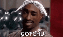 a man wearing a bandana and a necklace is smiling and says `` i gotchu '' .