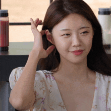 a woman in a floral dress holds her hand to her hair