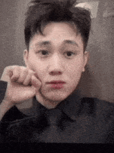 a young man in a black shirt and tie is taking a selfie with his hand to his face .