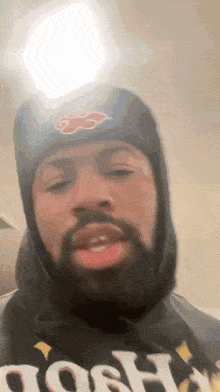 a man with a beard wearing a hat and a hoodie is talking .