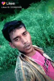 a man in a pink shirt is standing in front of a green bush