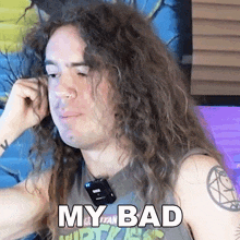 a man with long curly hair is wearing a shirt that says " my bad "