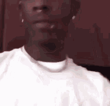 a close up of a man 's face wearing a white shirt and a silver chain around his neck .