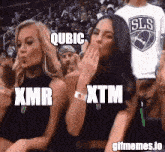 a group of women sitting in a stadium with xmr xtm and qubic written on their faces