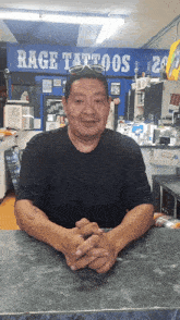 a man sits at a counter in front of a rage tattoos sign