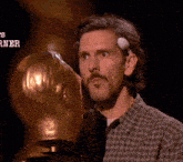 a man in a plaid shirt is holding a trophy with a ball on his forehead .