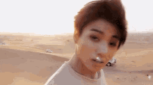 a young man is standing in the desert with a car in the background .